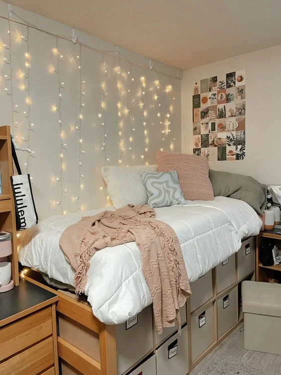This image is of a dorm room with lights, picture frames, and a chunky bedspread