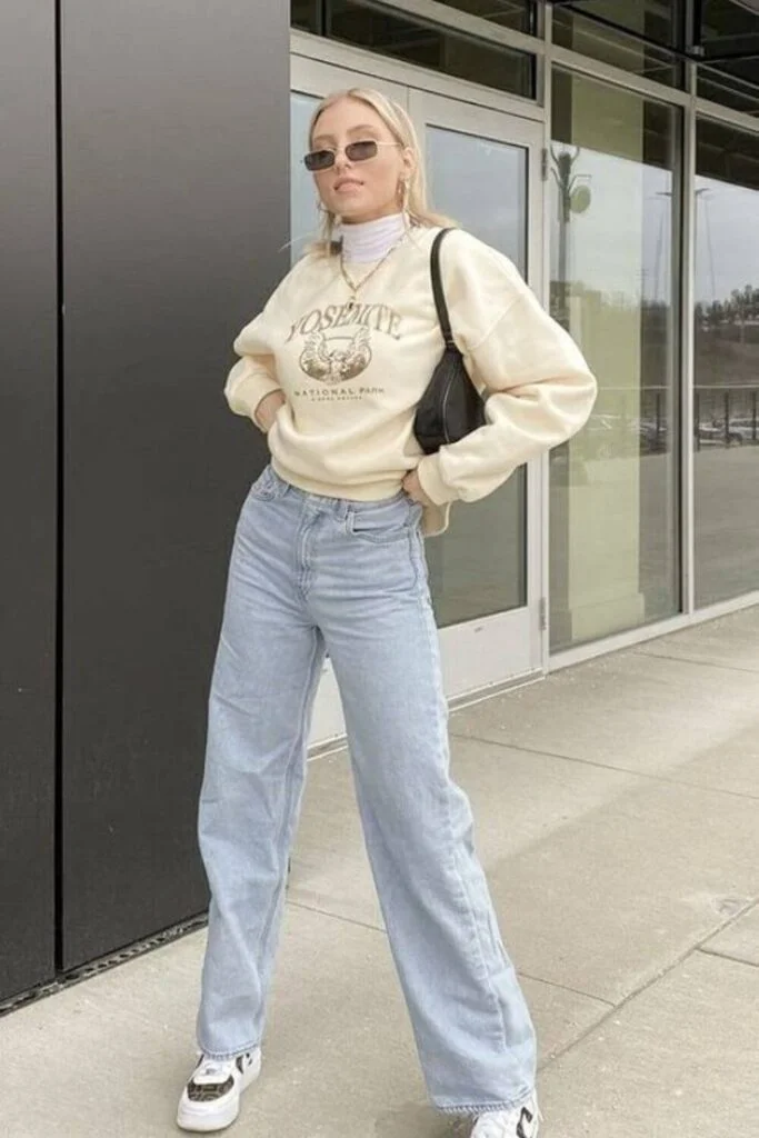 This image is of a back to school outfit of mom jeans and a cream colored sweatshirt with a black bag