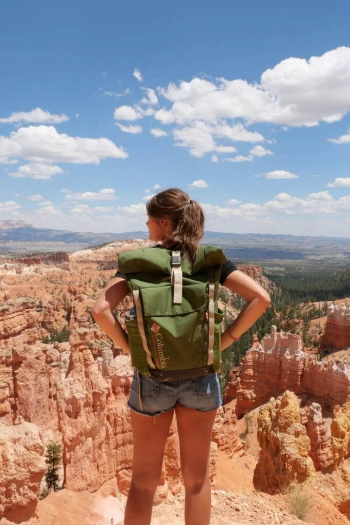 This image is of a college girl standing with a backpack overlooking a canyon after a hike. The backpack is green