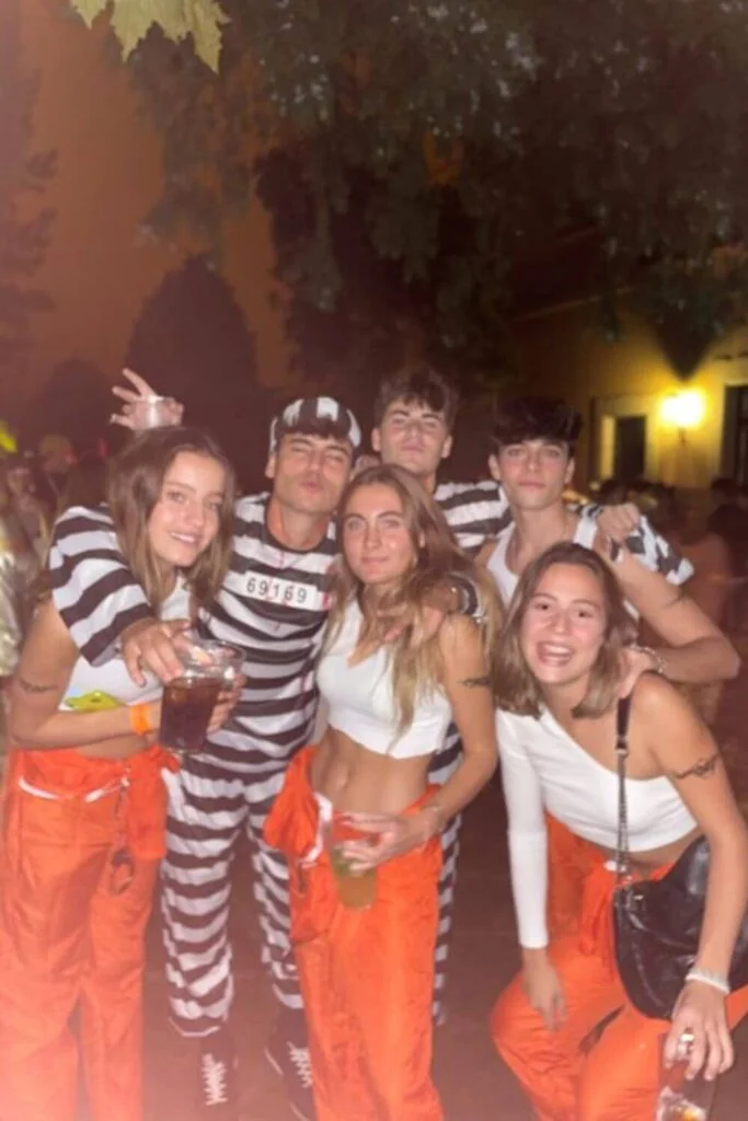 This image is of a group of college friends dressed up as prisoners and jailers for halloween. They are wearing all white tops and orange bottoms