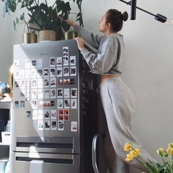This image is of a girl decorating her fridge with poloriods and plants