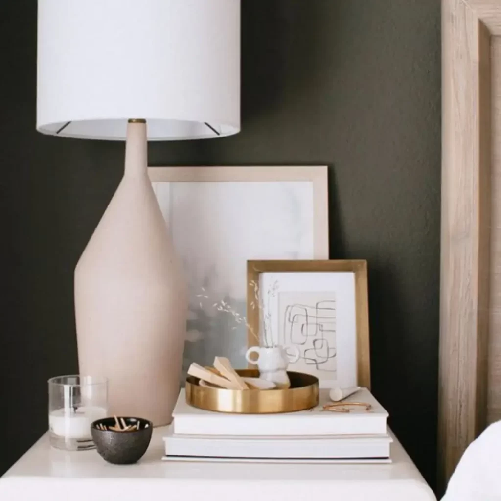 The photo is of a nightstand with a lamp, pictures, and a candle