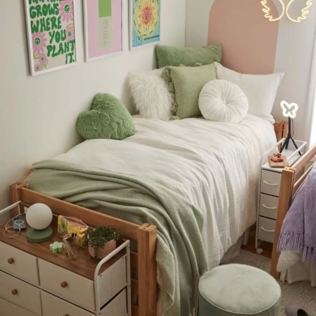 This photo is of a dorm bedroom decorated in sage green and white covers. There are desks and wall art.